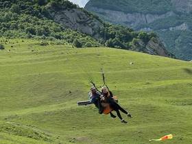 Tandem paragliding over a green slope