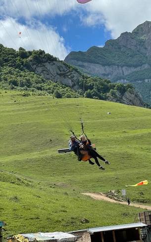 Tandem paragliding over a green slope