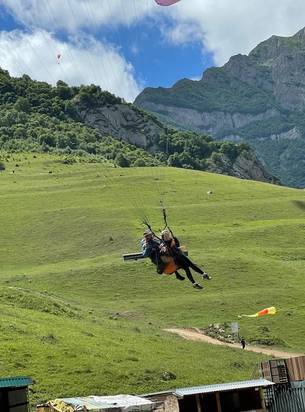 Tandem paragliding over a green slope